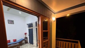A room with a checkered floor, a wooden bench, a small table with a vase, and a view of a balcony with a railing.