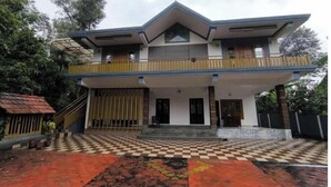 A two-story house with a balcony, a checkered entrance, and a tiled driveway.