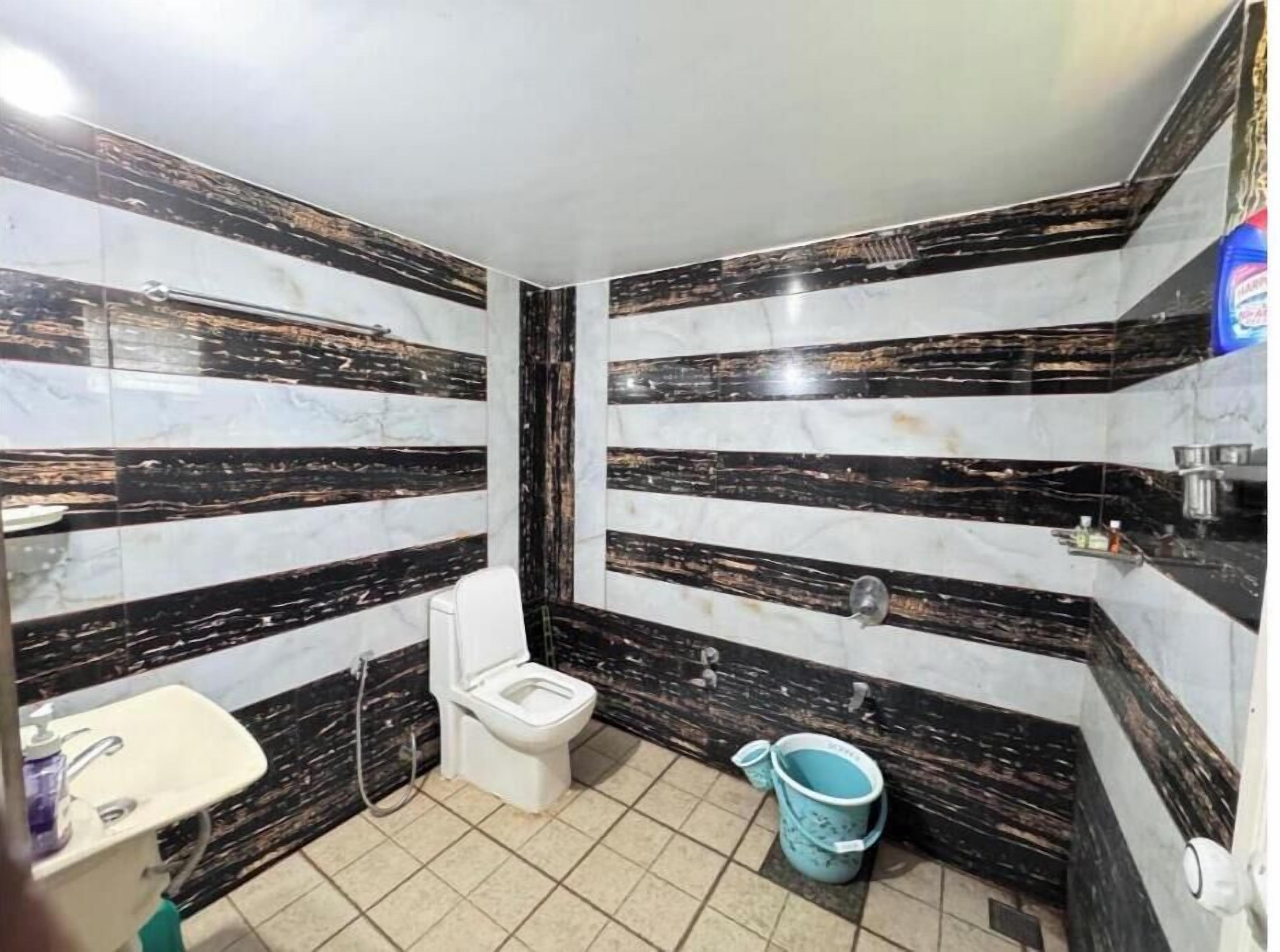 A bathroom with black and white marble walls, a toilet, a sink, and a blue bucket.