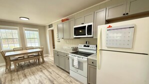 A modern kitchen with grey cabinets, a built-in microwave, a refrigerator, and a wooden dining table with chairs. - Relax with family and friends in this peaceful cabin right off the boat ramp! (Somerset)