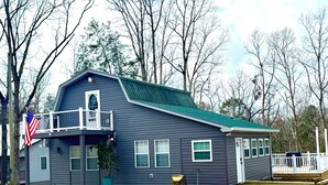 A two-story house with a balcony, a flag, and a green roof. - Relax with family and friends in this peaceful cabin right off the boat ramp! (Somerset)