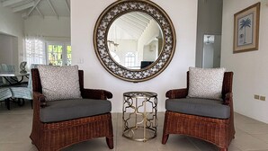 Una habitación con dos sillones de mimbre, un espejo redondo y una mesita auxiliar.