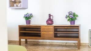 A wooden console table with a glass cabinet above it, a purple pitcher, and two potted plants with purple flowers.