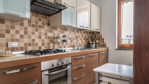 A modern kitchen with a gas stove, oven, and stainless steel appliances. There is a sink with a faucet, and the backsplash is made of checkered tiles. The cabinets are wooden with silver handles, and there is a window with a view of the outdoors.
