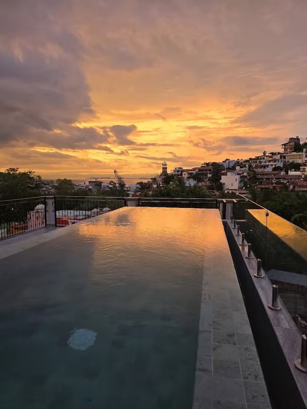A rooftop pool with a view of a cityscape during sunset.