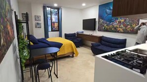 A compact hotel room with a bed, a desk, a sofa, and a kitchen area. - New studio Apt. in the coveted Zona Romantica with roof top pool (Puerto Vallarta)