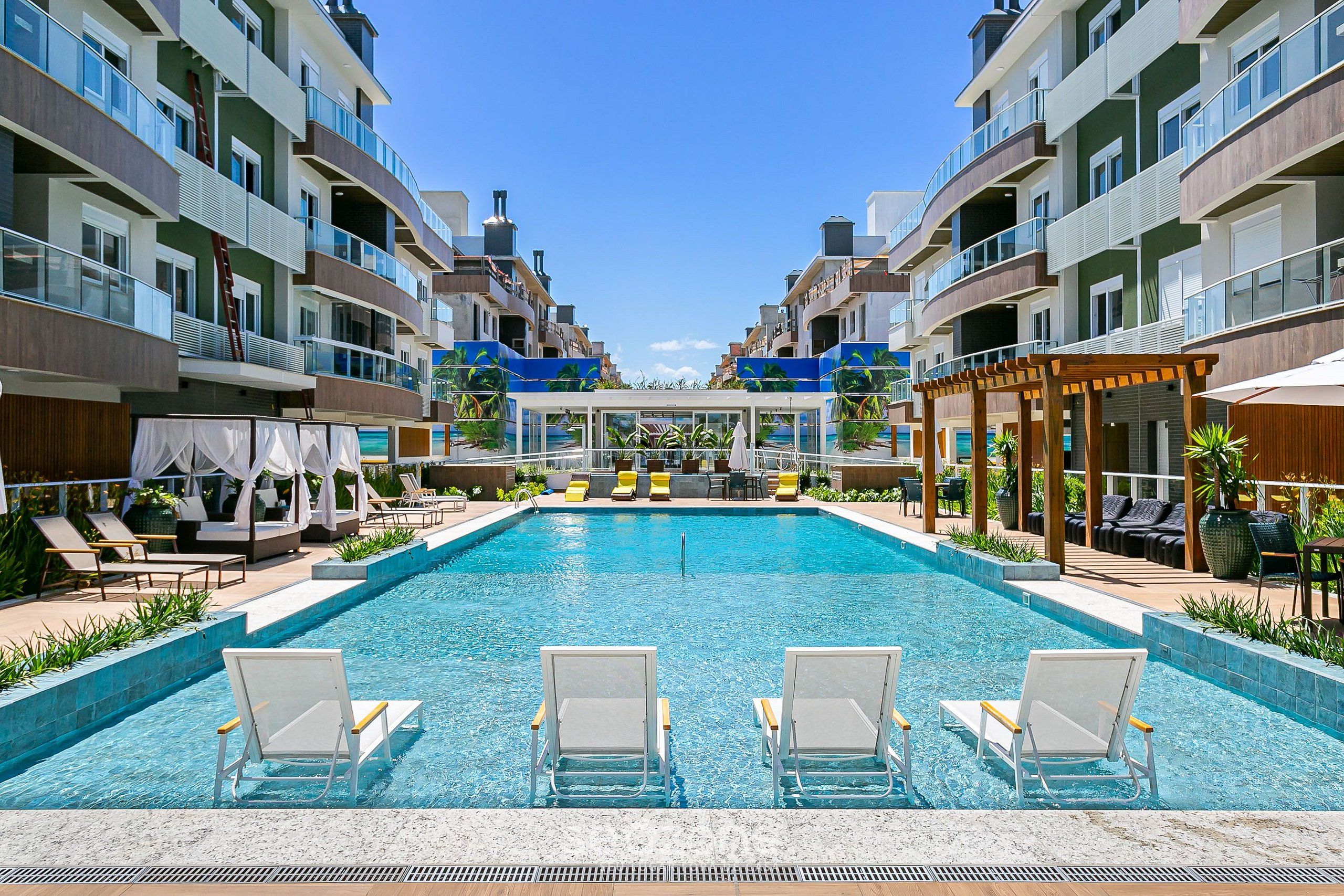 Una piscina con sillas de descanso, un área de estar techada y vistas a edificios de varios pisos.