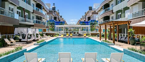 A swimming pool with lounge chairs, a covered seating area, and a view of multi-story buildings.