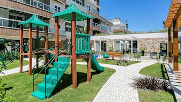 Un parque infantil con toboganes verdes y escaleras, rodeado de un camino pavimentado y vegetación.