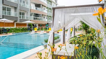 A swimming pool with lounge chairs and umbrellas, surrounded by a multi-story building with balconies.