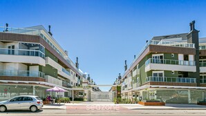 Un immeuble moderne à plusieurs étages, doté de balcons, d’une entrée couverte et d’une voiture garée devant.