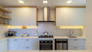 Cocina moderna con armarios blancos, horno empotrado, lavavajillas y cafetera.