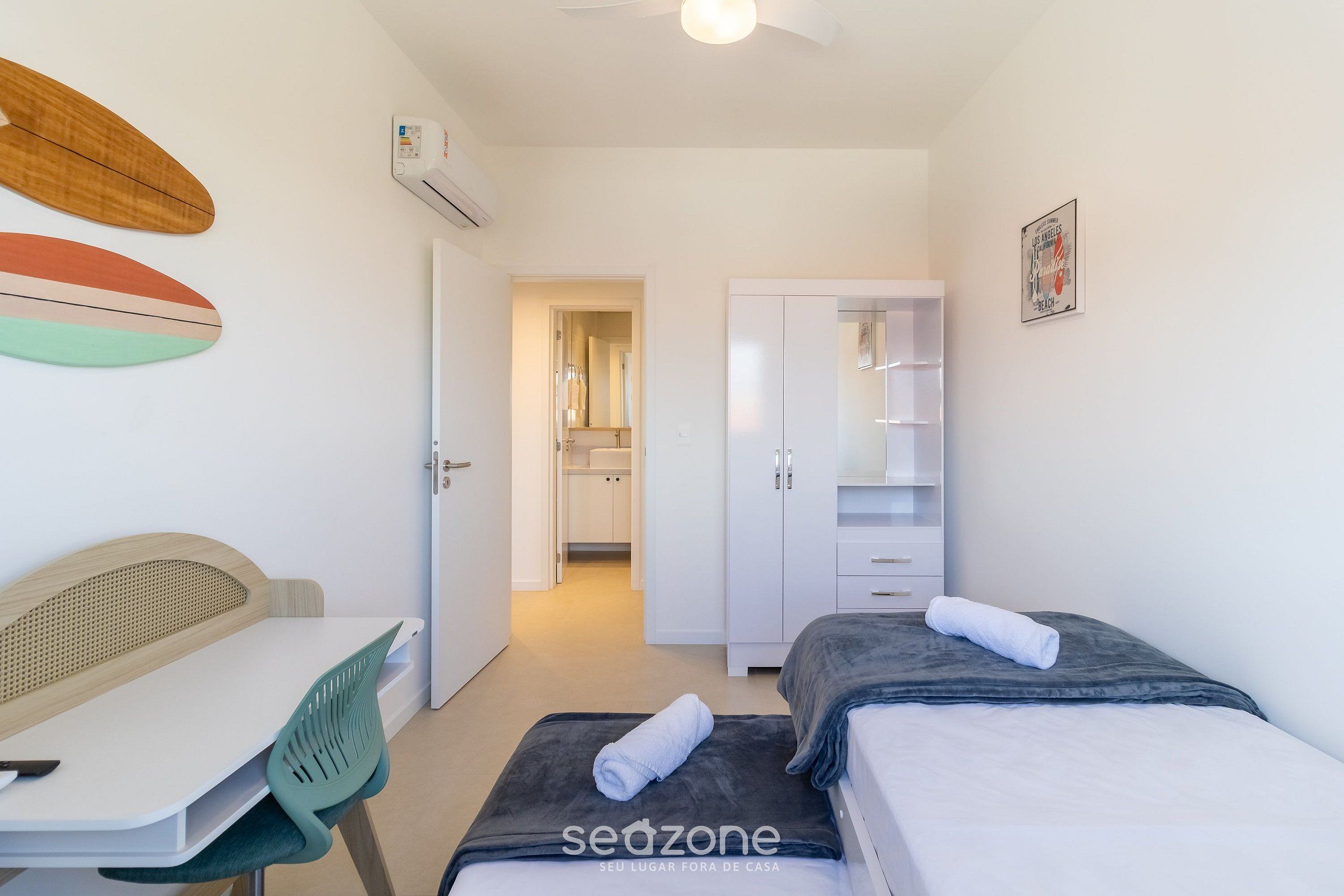 Un dormitorio moderno con dos camas, un escritorio y una silla. Hay un armario y una puerta que da a un baño.