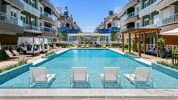 Une piscine dotée de chaises longues et d’un espace de repos couvert, le tout entouré d’immeubles à plusieurs étages avec des balcons.