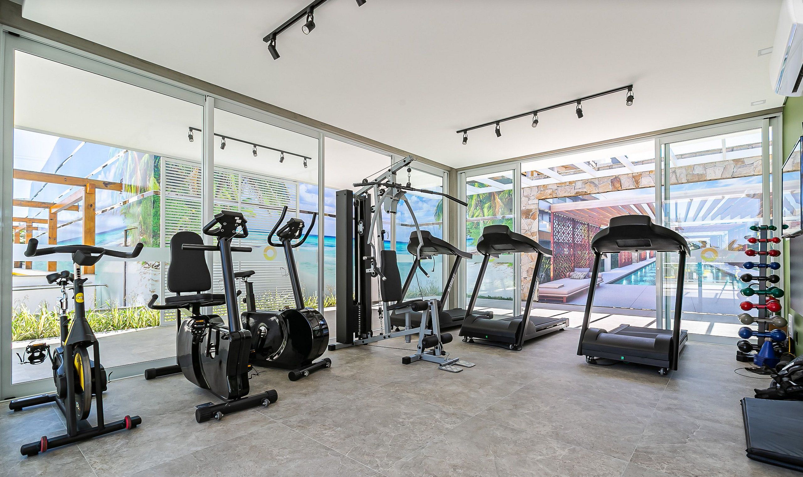 A modern gym with cardio machines, weightlifting equipment, and large windows offering views of the outdoors.