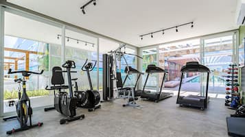 A modern gym with cardio machines, weightlifting equipment, and large windows offering views of the outdoors.