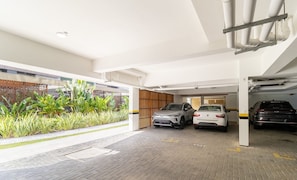 A covered parking area with two cars parked, a bamboo fence, and a paved walkway. - Seaside Condominium in Campeche-florianopolis SHR (Florianópolis)