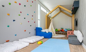 A child's playroom with a climbing wall, a blue sofa, a small table, and a TV mounted on the wall. - Seaside Condominium in Campeche-florianopolis SHR (Florianópolis)