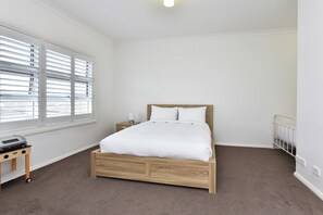 Quarto com cama de madeira, mesa de cabeceira, abajur e janela com persianas.