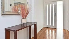 Un couloir avec une console en bois, un vase contenant des plantes séchées, un miroir et une porte à lattes verticales.