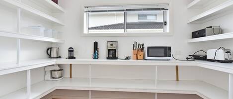 Cocina compacta con armarios blancos, una ventana sobre la encimera y diversos electrodomésticos, como una cafetera, microondas y tostadora.