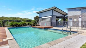 A swimming pool with a wooden deck, a covered seating area, and a stone building with a grey roof.