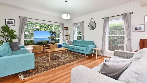 A modern living room with a large TV, a teal sofa, a grey sofa, and a wooden coffee table.