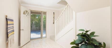 A hallway with a white door, a staircase, and a potted plant.