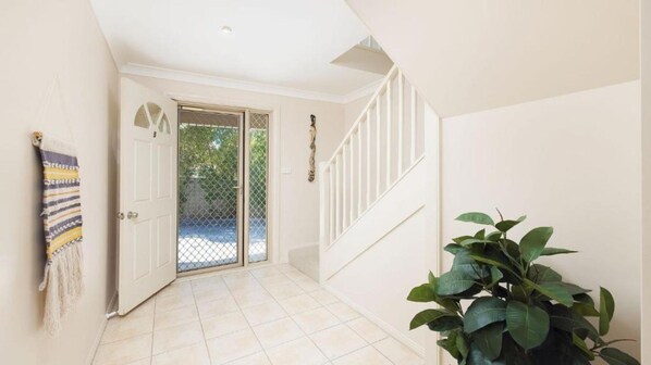 A hallway with a white door, a staircase, and a potted plant.