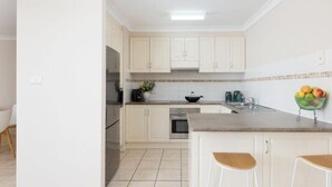 Eine moderne Küche mit weißen Schränken, einem Edelstahl-Kühlschrank, einer Spüle und einer Obstschale auf der Arbeitsplatte.