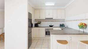 A kitchen with white cabinets, a stainless steel refrigerator, a sink, and a bowl of fruit on the counter.