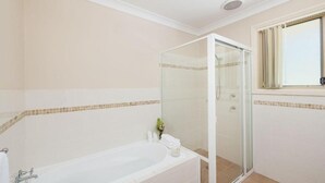 Ein Badezimmer mit einer Glaskabine zur Dusche, einer weißen Badewanne und einem Fenster mit Jalousien.