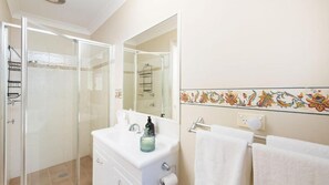 A bathroom with a glass shower enclosure, a white sink with a mirror, and a decorative tile border.