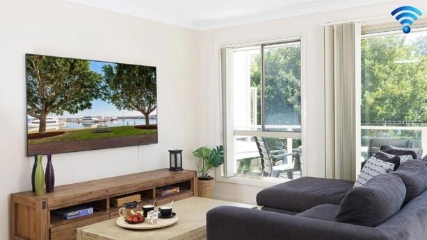 A living room with a large window, a sofa, a coffee table with a tray of fruit, and a painting of trees. - Tomaree Escape Family GetawayIn Nelson Bay (Nelson Bay)