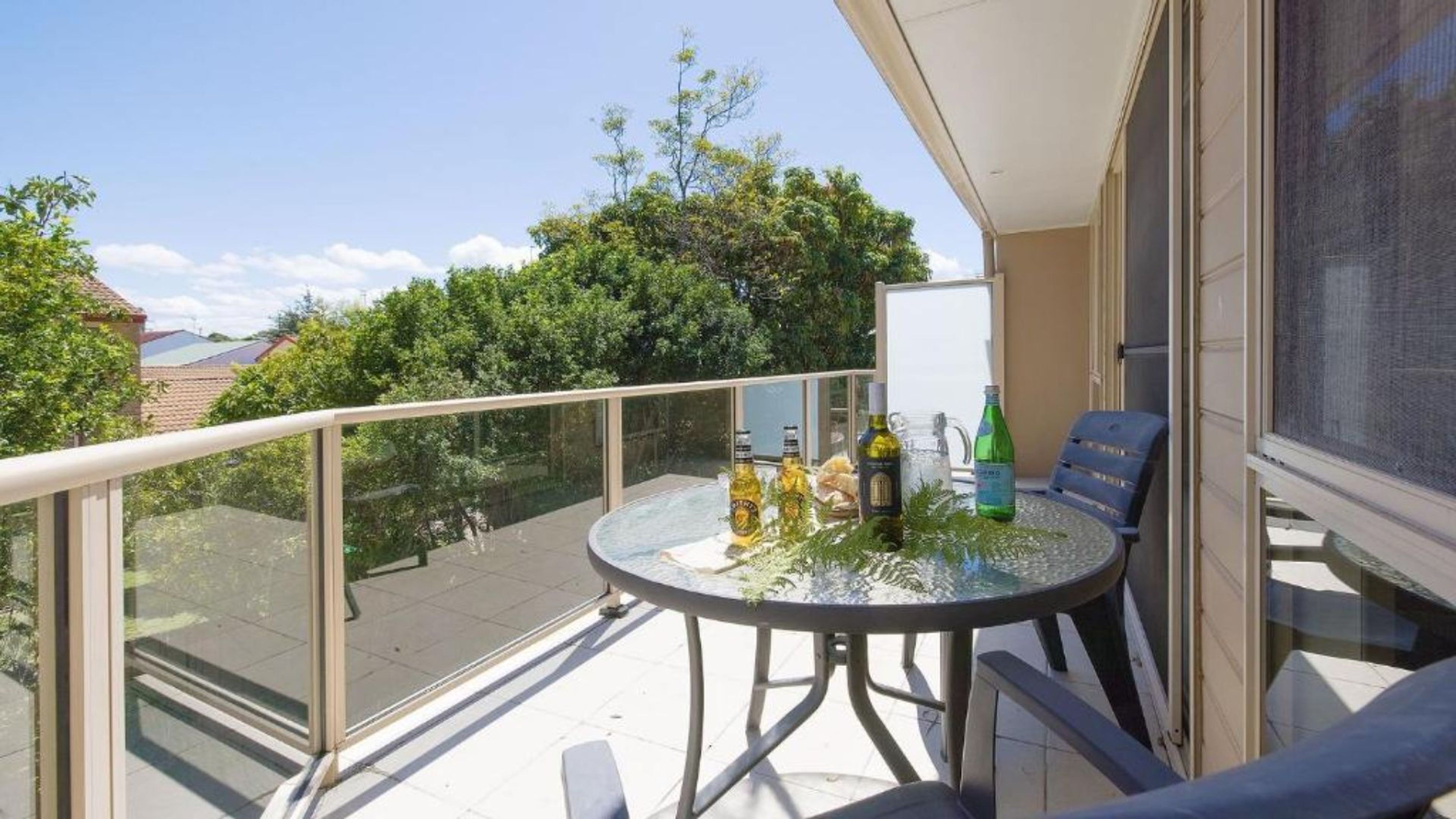 A balcony with a glass table, chairs, and bottles.