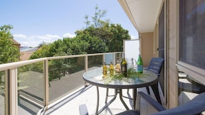 Een balkon met een glazen tafel, stoelen en flessen.
