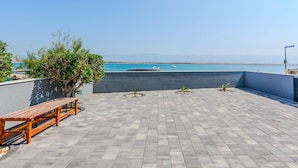 Una terraza en la azotea con vistas al mar, un banco de madera y plantas en macetas.