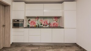 Una cocina compacta con muebles blancos, horno empotrado y salpicadero con diseño floral.