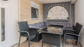Un rincón al aire libre acogedor con mobiliario de mimbre, un banco acolchado y una pared decorativa con una red y adornos colgantes.