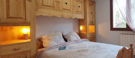 A bedroom with a wooden headboard, a bed with a white comforter, and built-in wooden cabinets with heart-shaped cutouts.