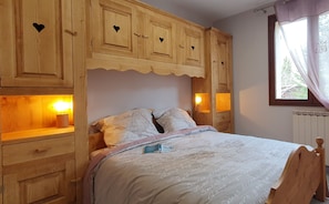 A bedroom with a wooden headboard, a bed with a white comforter, and built-in wooden cabinets with heart-shaped cutouts. - Chalet T6 confort proche Station (Dévoluy)