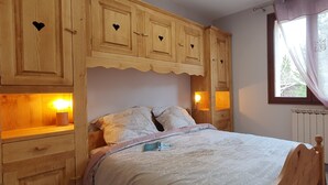 A bedroom with a wooden headboard, a bed with a white comforter, and built-in wooden cabinets with heart-shaped cutouts. - Chalet T6 confort proche Station (Dévoluy)
