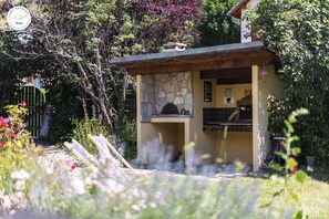 Un edificio de piedra con un pequeño porche, rodeado de abundante follaje y un sendero en el jardín.