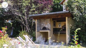 A stone building with a small porch, surrounded by lush greenery and a garden path. - Chalet T6 confort proche Station (Dévoluy)