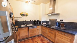 A modern kitchen with wooden cabinets, a stainless steel range hood, and a black countertop. - Chalet T6 confort proche Station (Dévoluy)