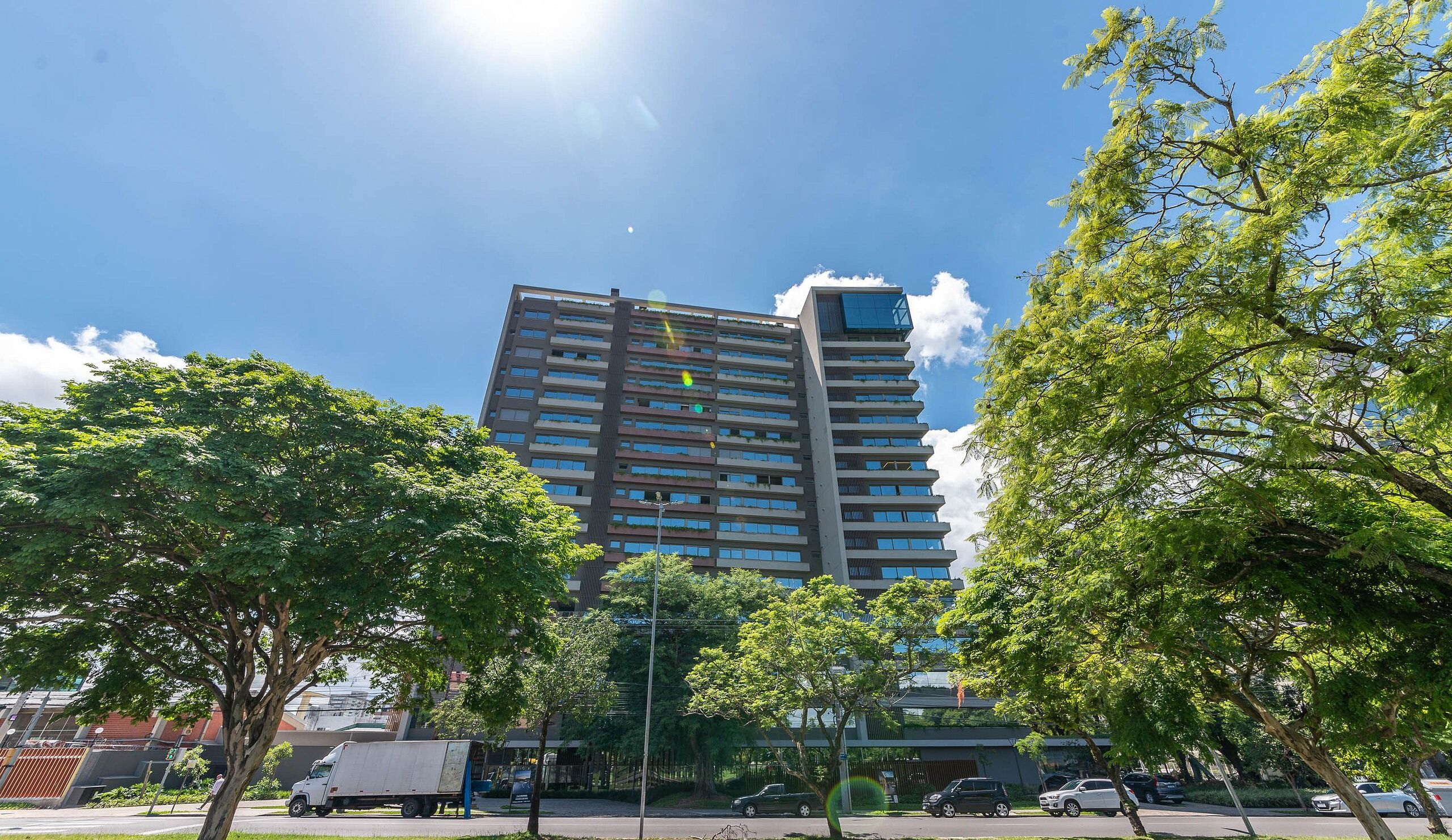 A high-rise building with multiple floors, surrounded by trees and parked cars.
