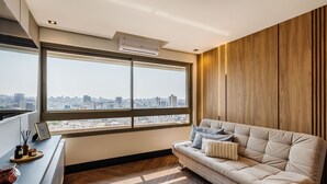 Een moderne woonkamer met een groot raam, een bank en een houten wandpaneel.