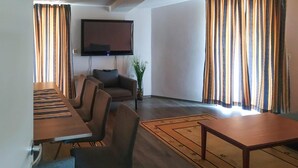Una sala de estar con una televisión de pantalla plana montada en la pared, un sofá, una mesa de centro y una mesa de comedor con sillas.