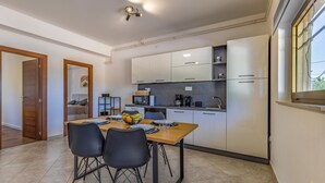 A modern kitchen with white cabinets, a dining table with four chairs, and a coffee maker.