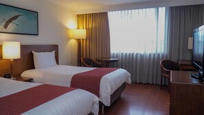 Una habitación de hotel con dos camas, un escritorio, una silla, una lámpara y un televisor.